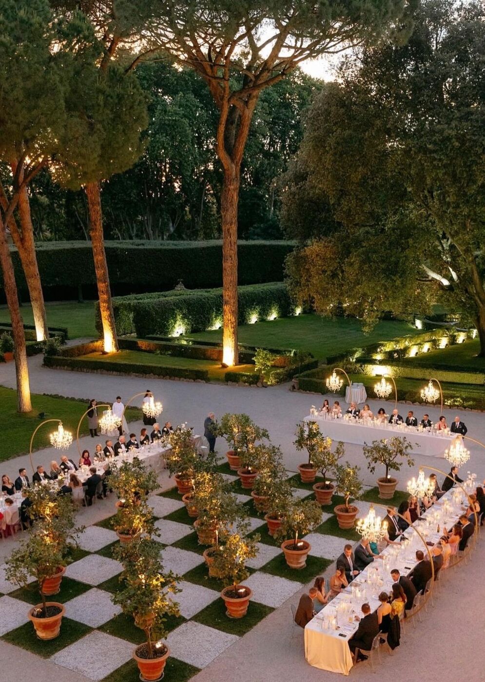 Cena di gala in giardino con lampadari, limoni in vaso e tavolate illuminate